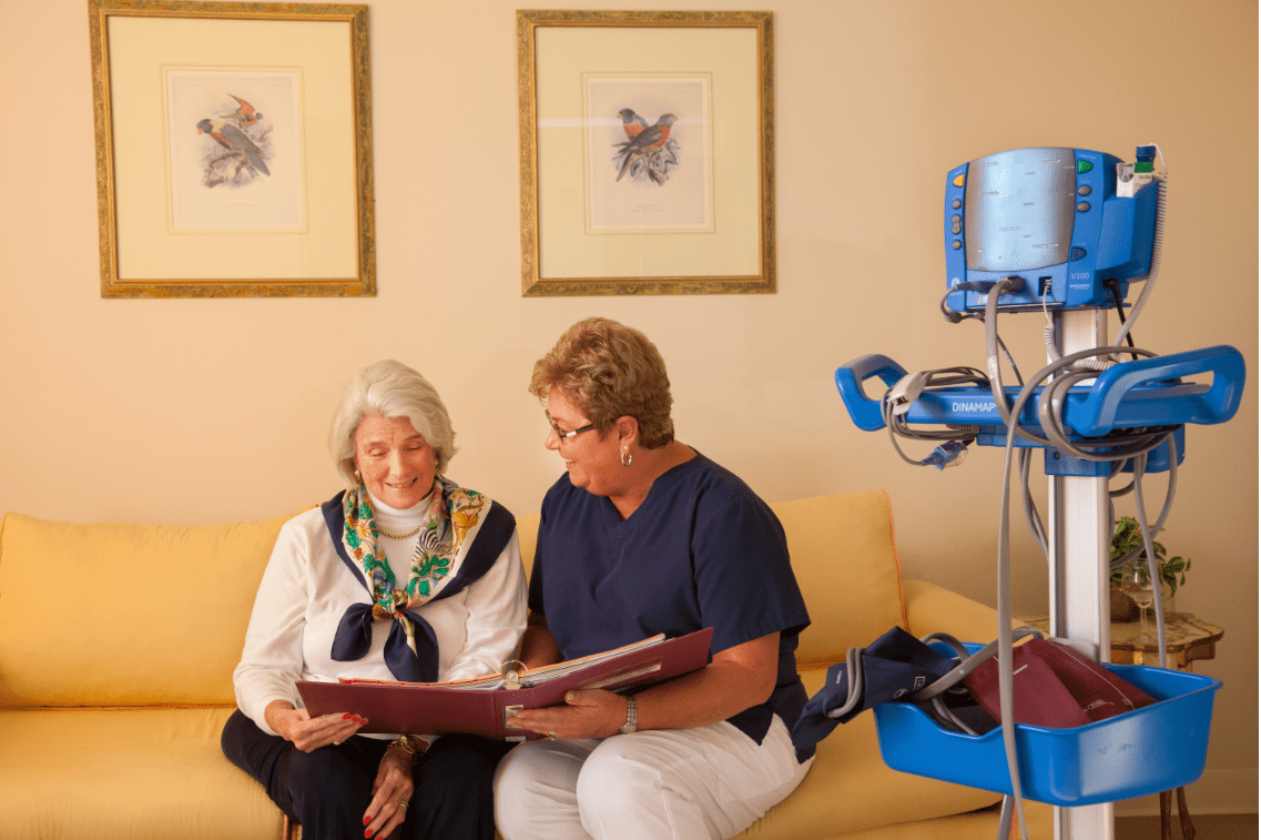A caregiver and an elderly woman sitting together, reviewing a photo album in a healthcare setting.