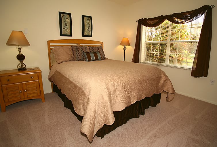 A cozy bedroom with a neatly made bed, soft lighting from a lamp, and a window adorned with curtains.