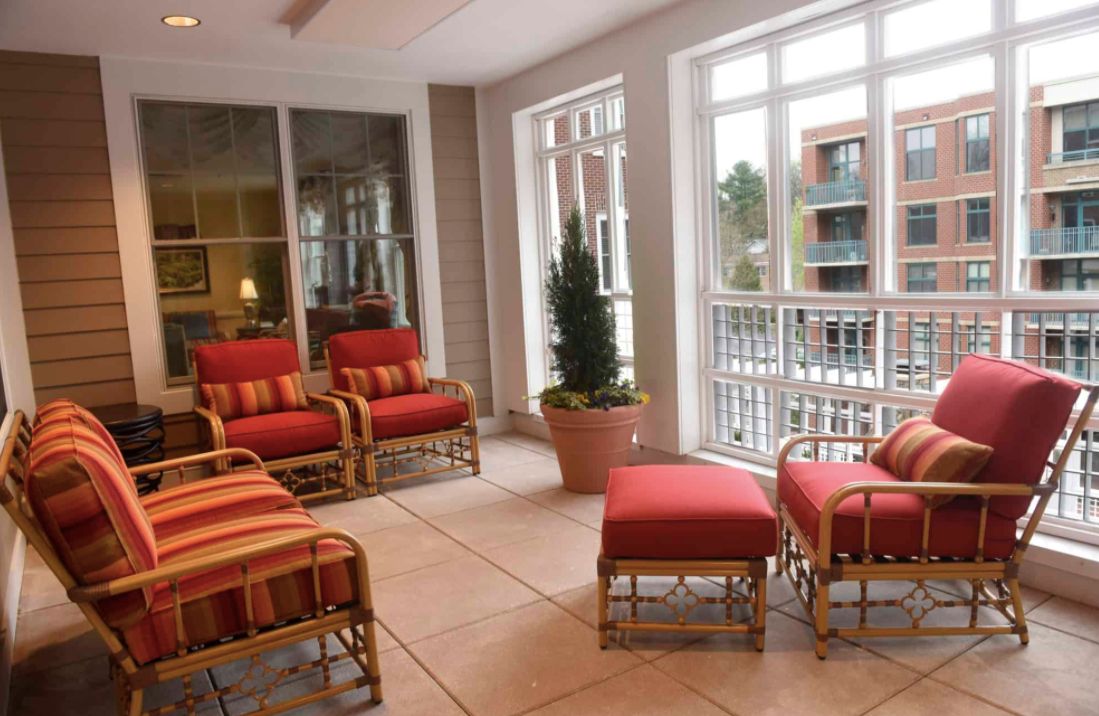 A sunlit seating area with comfortable chairs and ottomans near large windows.