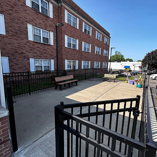 A view of a brick apartment building with a fenced courtyard and a bench.