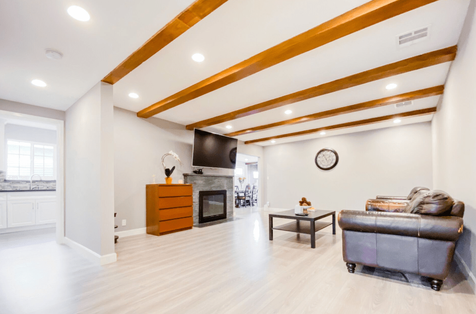 A modern and cozy living room featuring exposed wood beams, a fireplace, and minimalist decor.