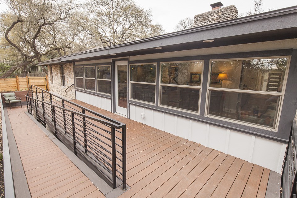 A view of a house with a spacious deck and railing, featuring large windows and surrounded by trees.