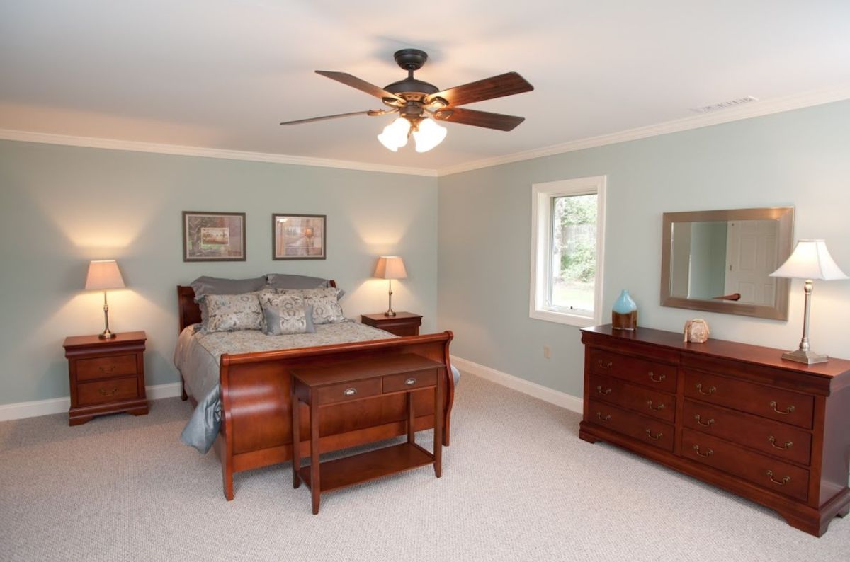 A cozy bedroom with a wooden bed, matching dresser, and a ceiling fan.