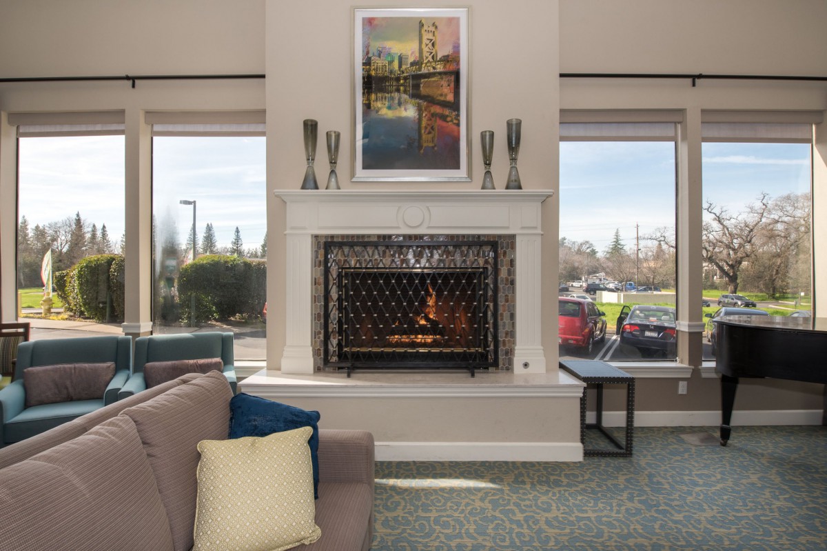 A modern living room with a cozy fireplace, featuring stylish decor and large windows.