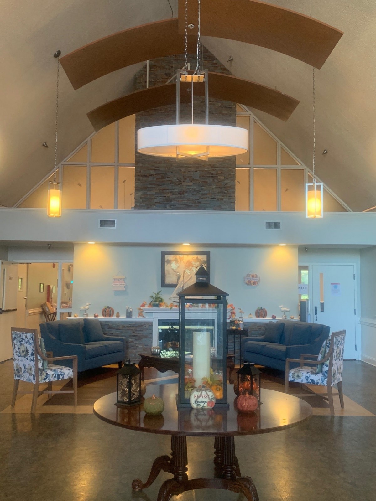 A modern living room with high ceilings, featuring a central chandelier, two blue sofas, and a round coffee table adorned with decorative items.
