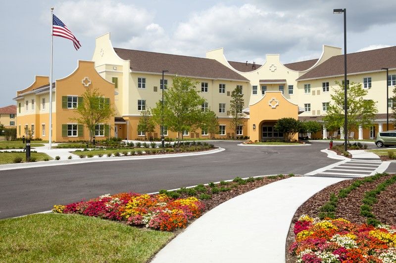 A well-maintained building with a landscaped entrance featuring vibrant flowers and an American flag.