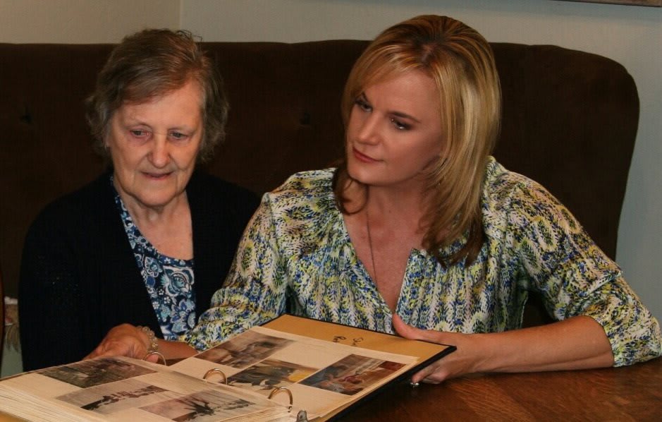 An elderly woman and a younger woman bonding over a photo album, sharing memories together.