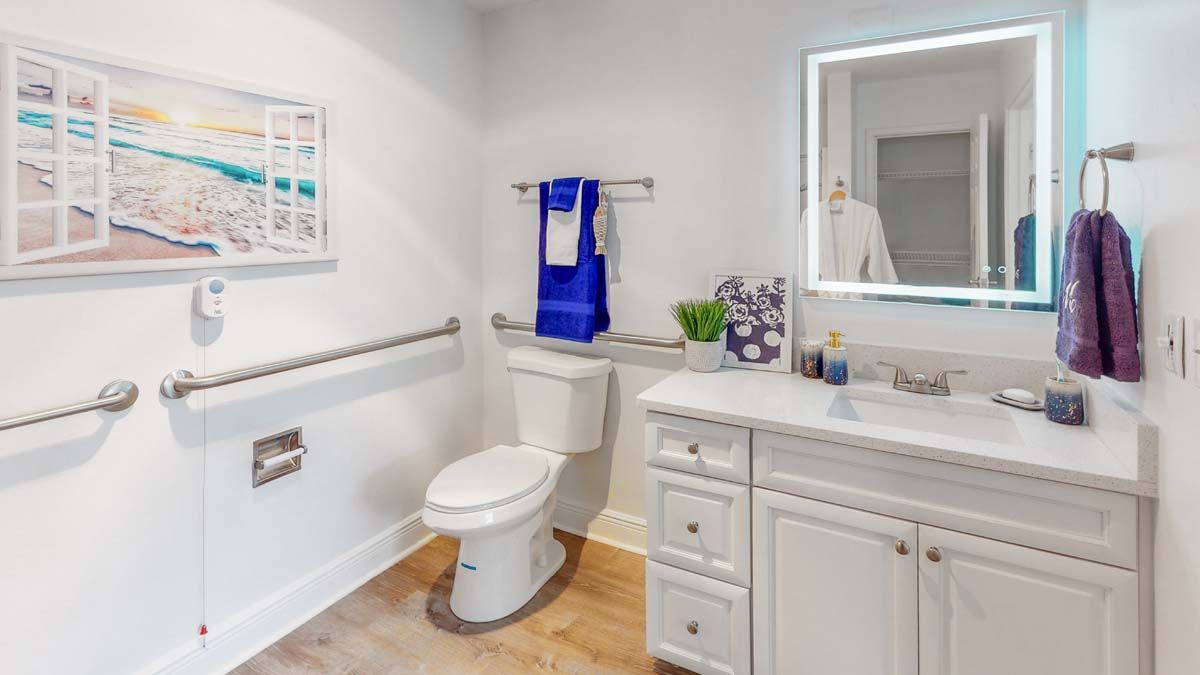 A clean and modern bathroom with white fixtures, a toilet, sink, and a lighted mirror.