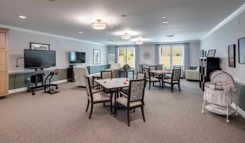 A spacious dining area with multiple tables and chairs, featuring a television and large windows.