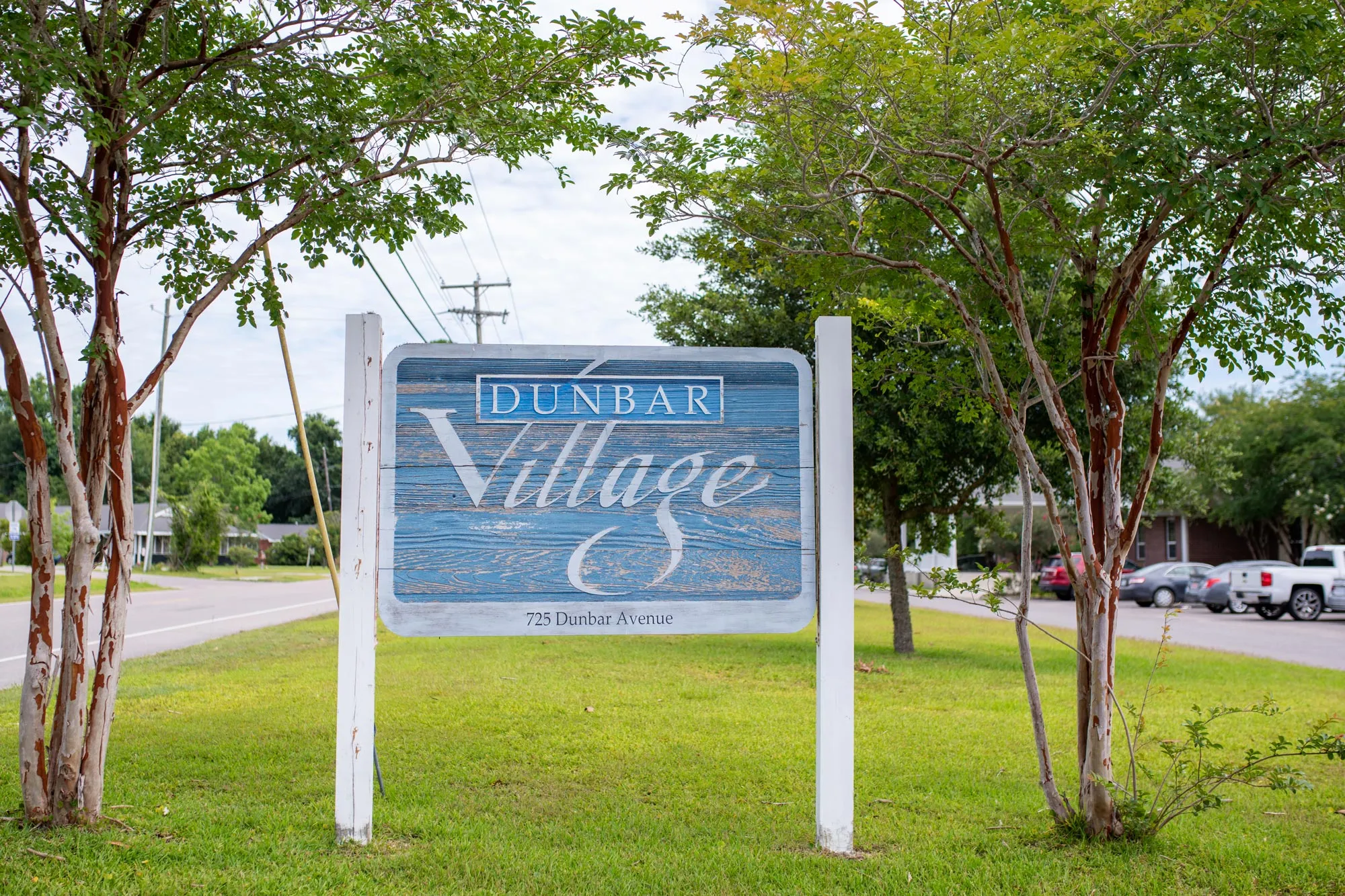 A wooden sign for Dunbar Village standing beside a grassy area with trees.
