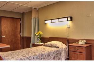A hospital room with a single bed, flowers on the bedside table, and soft lighting.