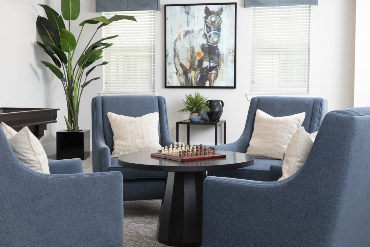 A modern living room with blue armchairs, a chess board on the table, and wall art creating a cozy atmosphere.