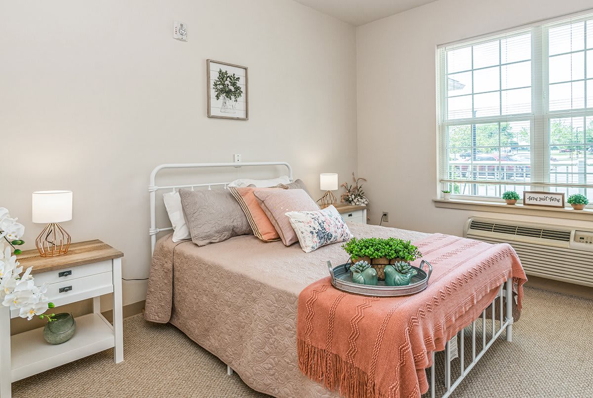 A cozy bedroom with a neatly made bed, decorative pillows, and a soft coral blanket.