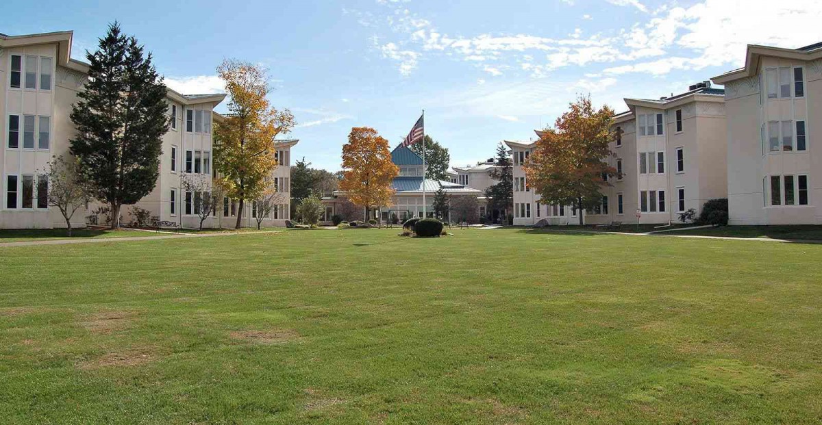 A college campus with buildings, a large lawn, and trees under a blue sky.