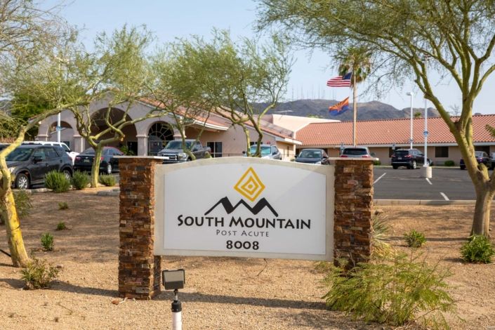 A sign for South Mountain with a building and mountains in the background.