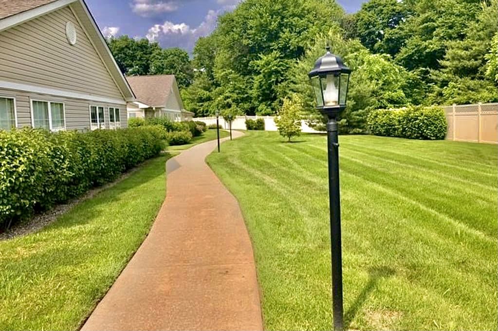 A well-maintained pathway with lamp posts and a lush green lawn in a suburban setting.