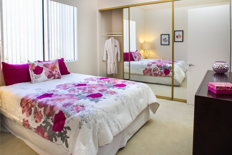 A cozy bedroom with floral bedding and a mirrored closet door.