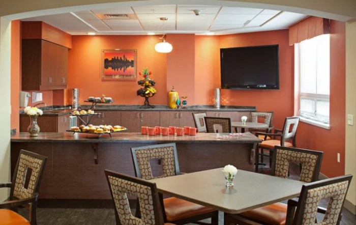 A modern restaurant interior showcasing neatly arranged tables and chairs, with a buffet counter in the background.