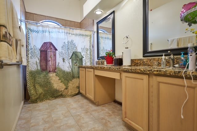A cozy bathroom with a decorative shower curtain, wooden vanity, and granite countertop.