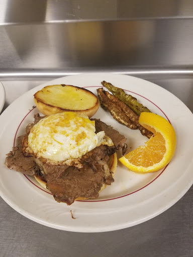 A hearty breakfast sandwich featuring tender beef, a fried egg, and served with orange slices.