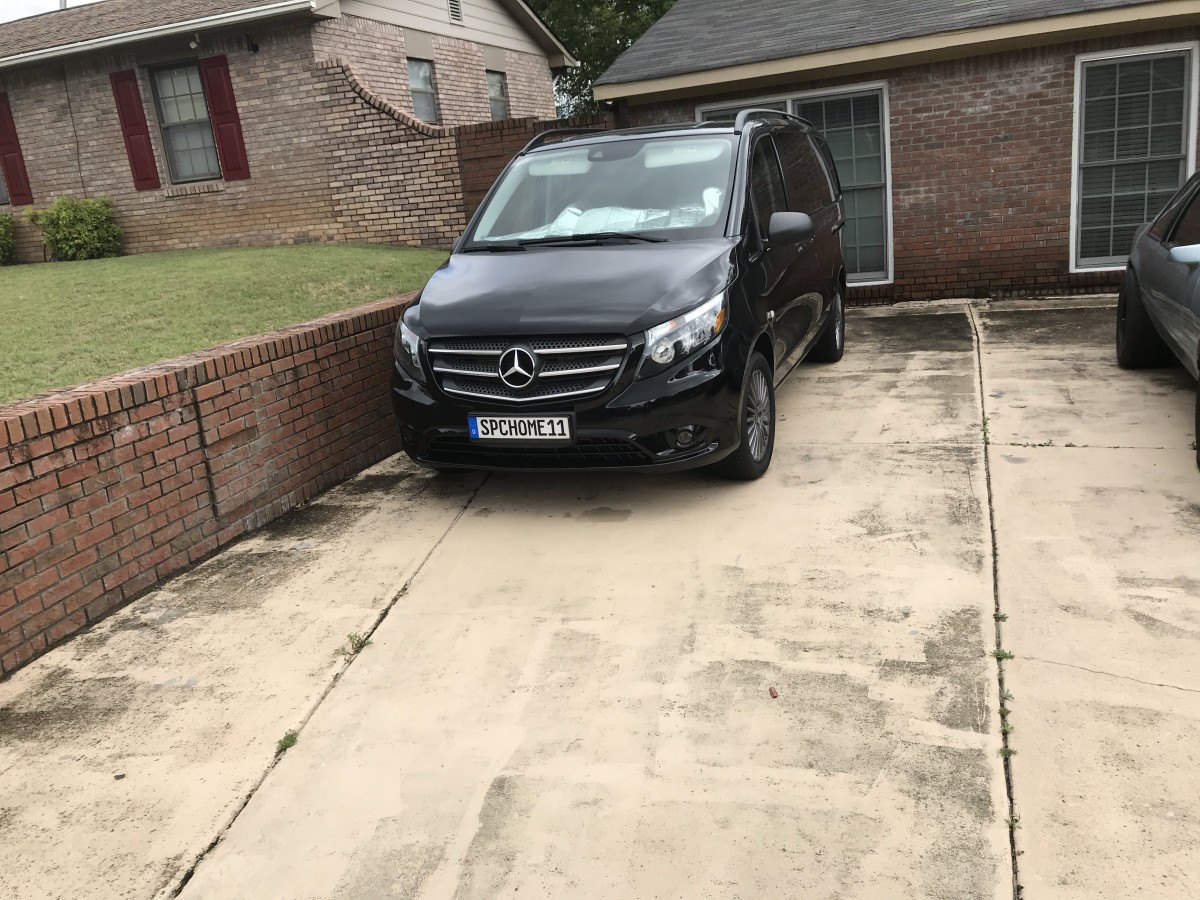 A black Mercedes-Benz van parked in a driveway next to a brick wall and house.