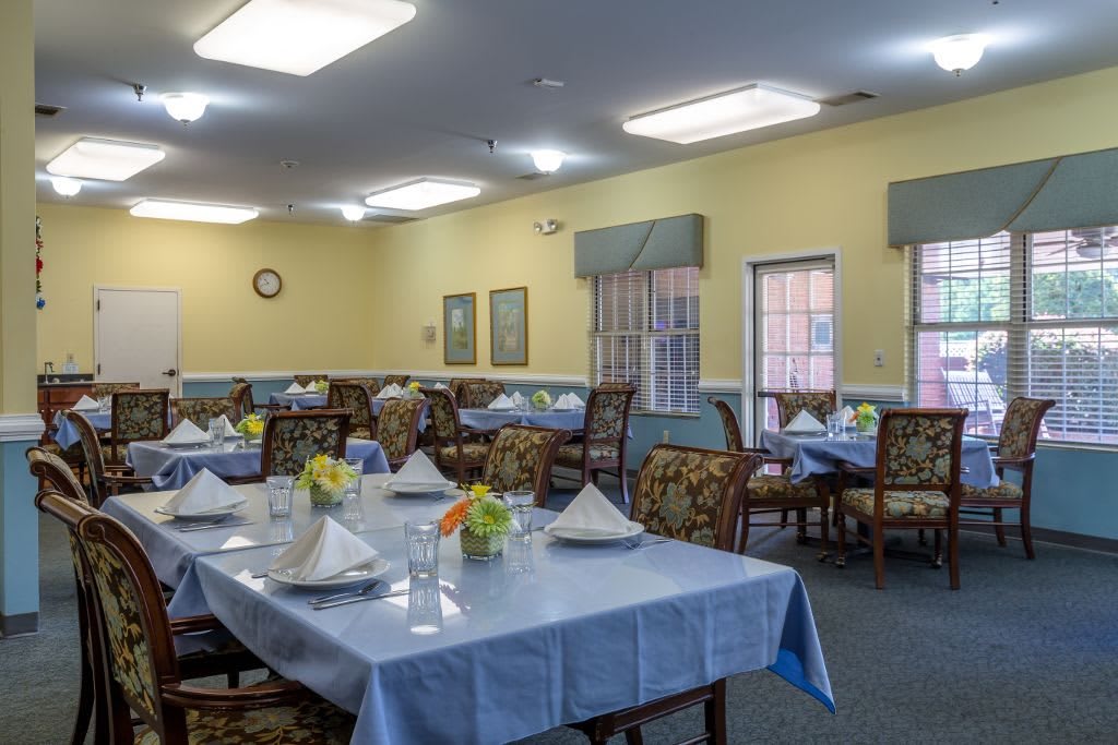 A well-arranged dining room with tables set for a meal, featuring floral centerpieces and neatly folded napkins.