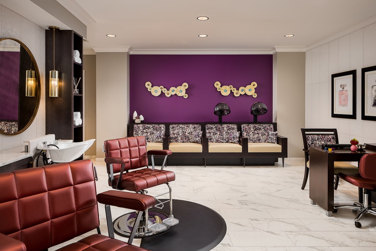 A stylish salon waiting area featuring red chairs and a purple accent wall.