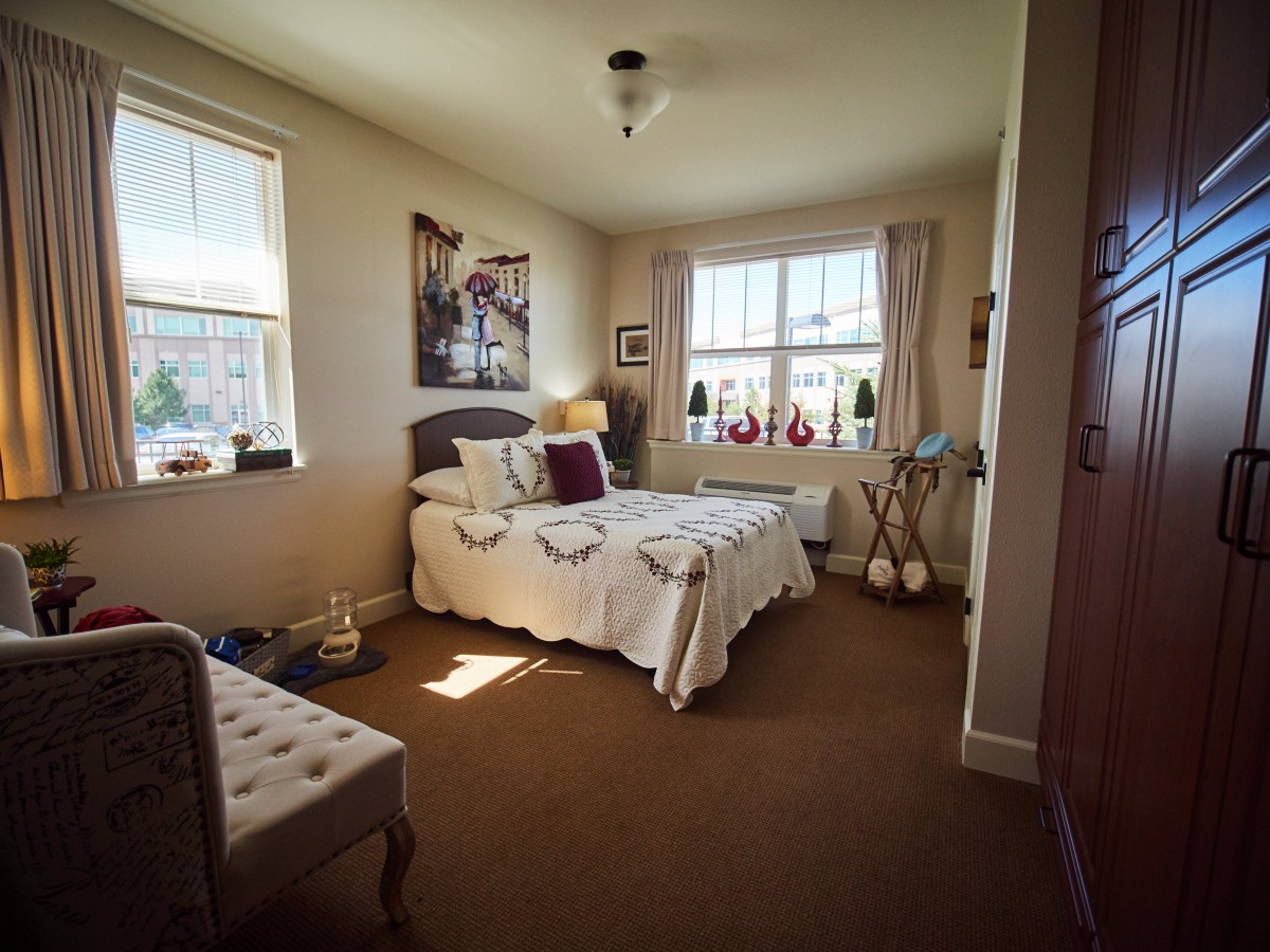 A cozy bedroom with a neatly made bed and ample natural light from two windows.