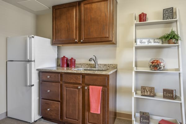 A small kitchen area featuring wooden cabinets, a granite countertop with a sink, open shelves, and a white refrigerator.