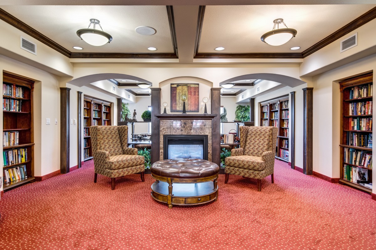 A cozy library with a central fireplace, surrounded by armchairs and bookshelves.