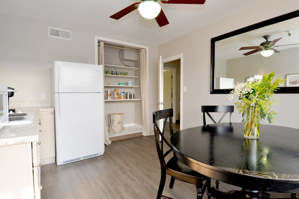 A modern kitchen dining area featuring a round black table with chairs, an open pantry, and a white refrigerator.