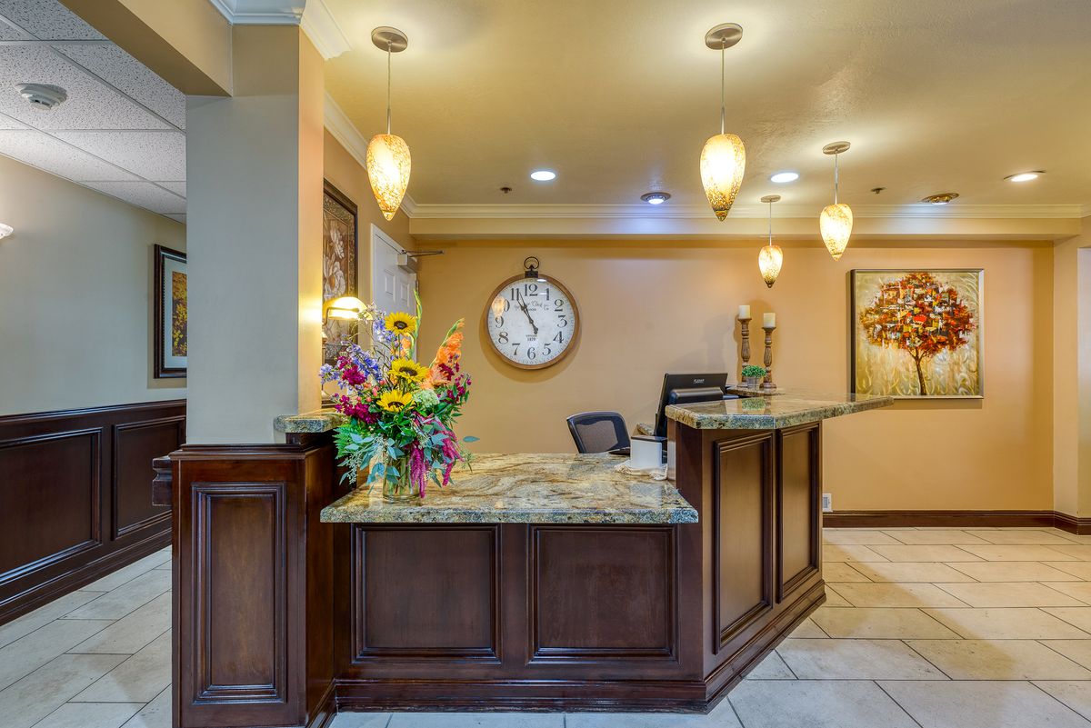 A hotel reception desk with decorative flowers and a wall clock.
