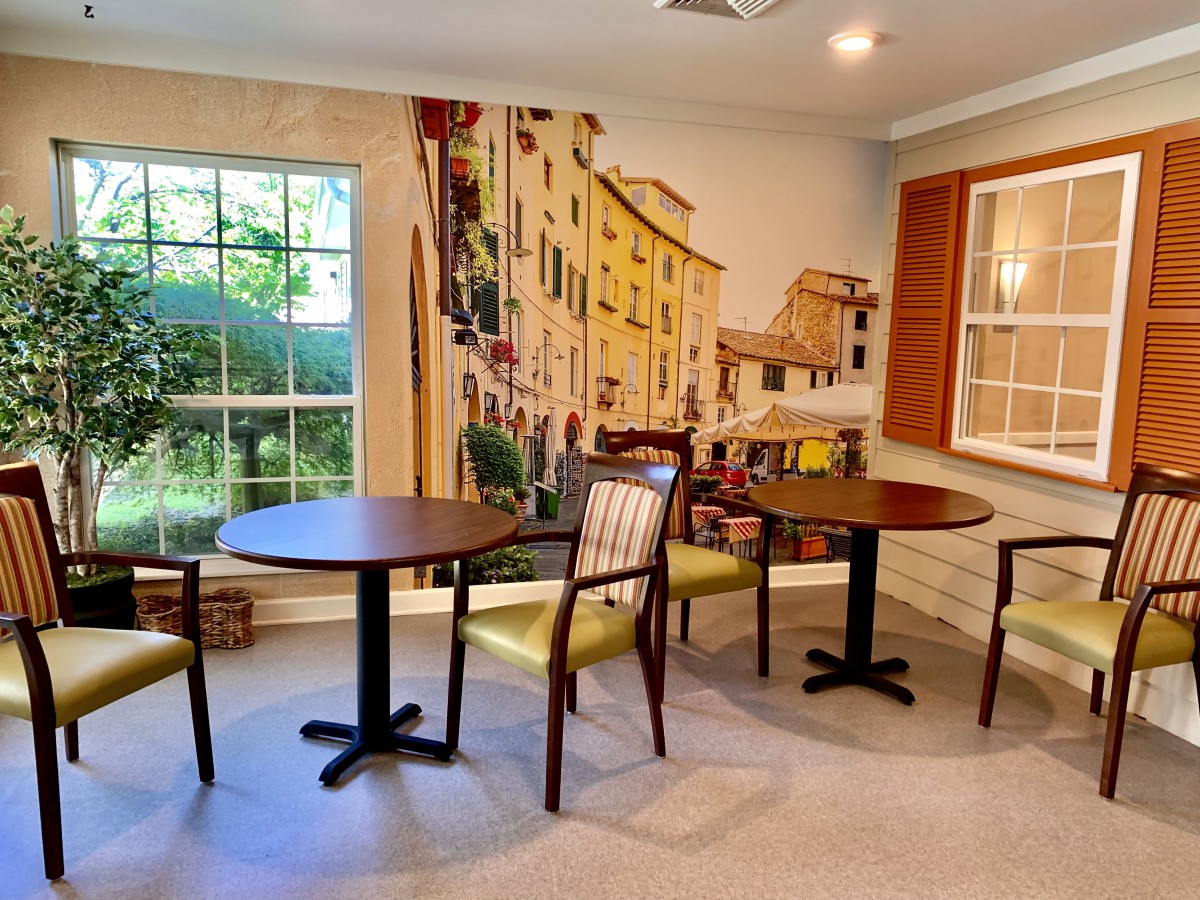 A cozy indoor seating area with tables and chairs, featuring a mural and a large window.