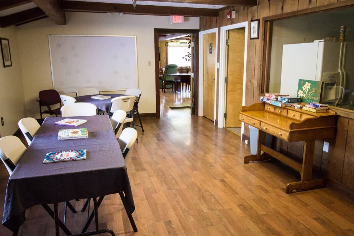 A meeting room with tables and chairs, featuring a whiteboard and wood floors.