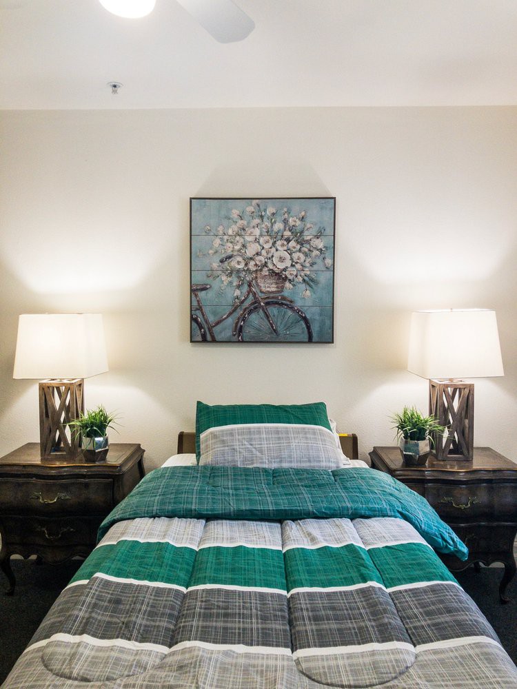 A cozy bedroom with a neatly made bed, flanked by nightstands and lamps, complemented by a floral artwork above the headboard.