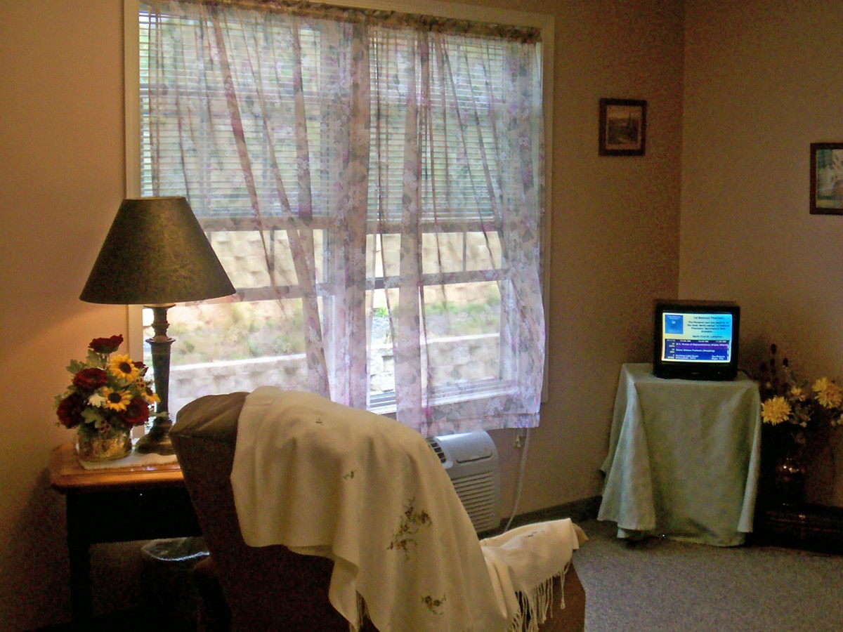 A cozy living room with a large window, sheer curtains, and a small television.