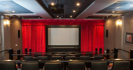 An empty cinema hall with red curtains and a large movie screen.