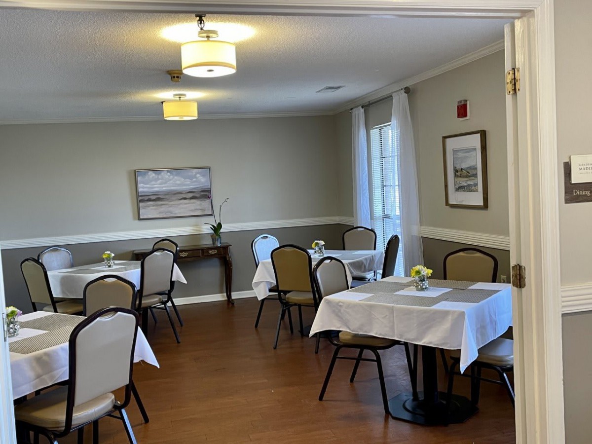 A cozy dining room with neatly arranged tables and chairs, decorated with paintings and bright lighting.