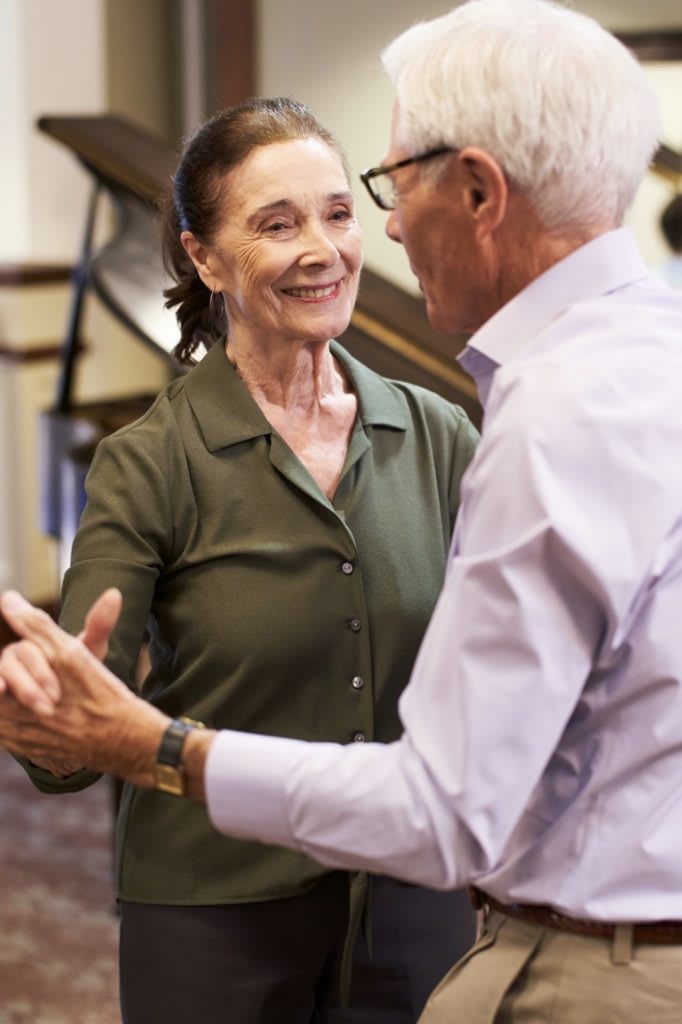 An elderly couple enjoys dancing together indoors.