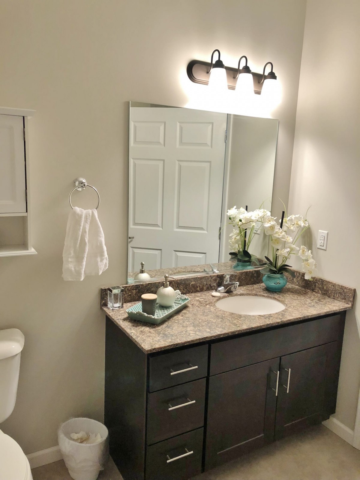 A neatly organized bathroom with a stylish vanity and mirror, decorated with flowers and towels.