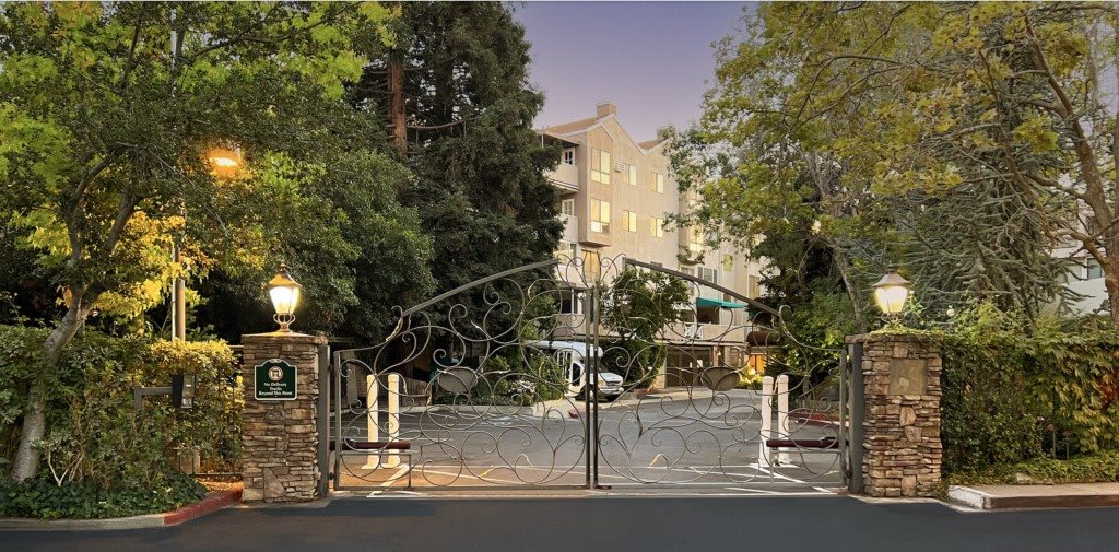 A gated entrance to a multistory residential building surrounded by trees during the evening.