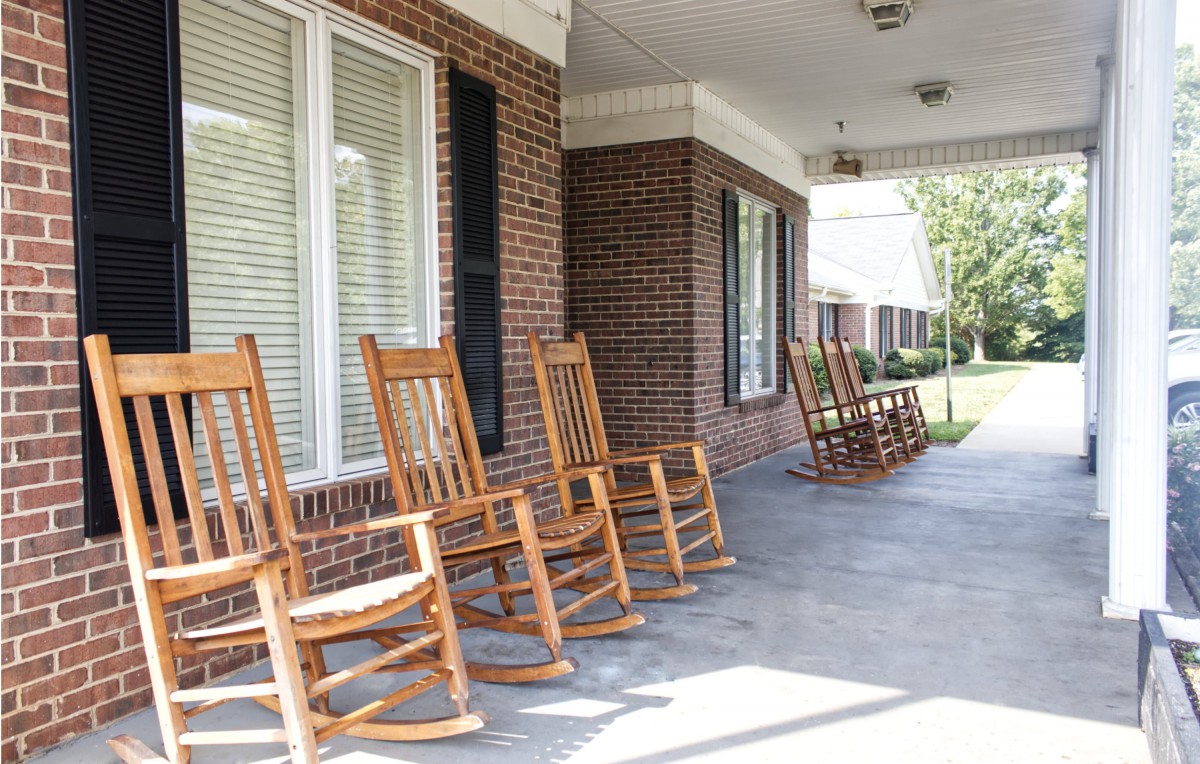 A row of wooden rocking chairs lined up on a brick porch, inviting relaxation.