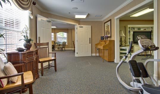 A well-lit hallway with a bench, piano, and open doors leading to a seating area.