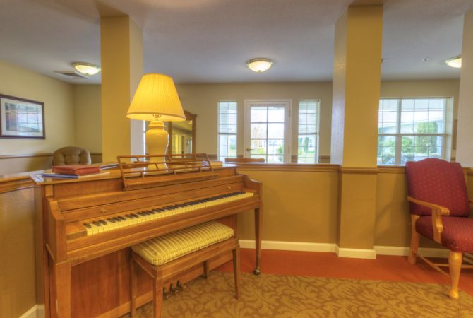 A cozy living room with a piano and lamp situated by large windows.
