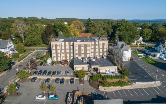 Aerial view of a hotel with a parking lot and surrounding greenery.
