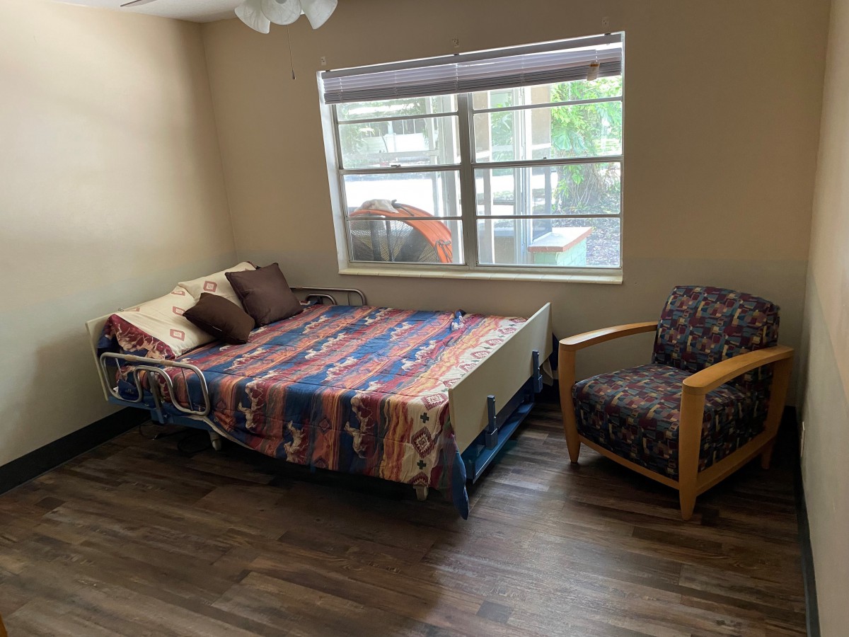 A cozy bedroom with a colorful bedspread, chair, and large window.