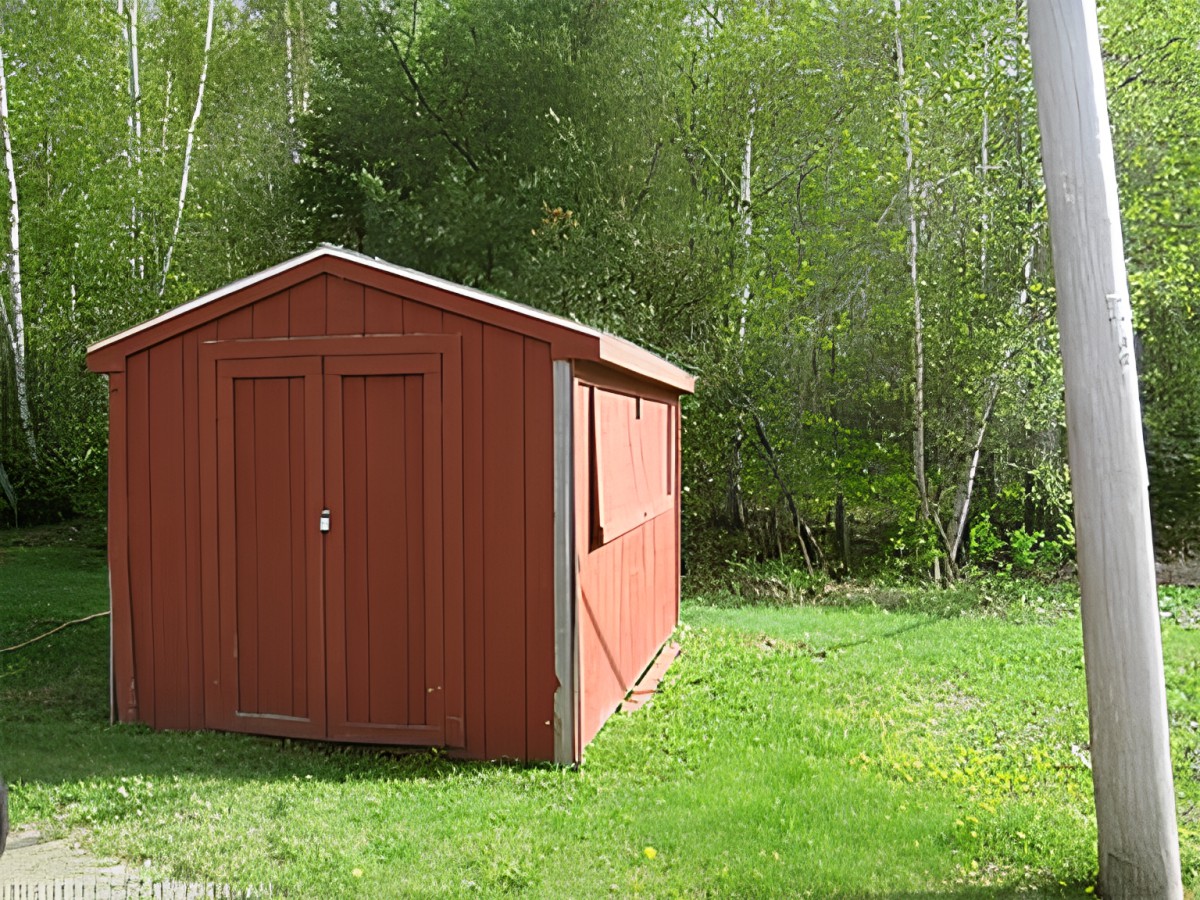 A wooden shed surrounded by lush greenery and a grassy lawn.