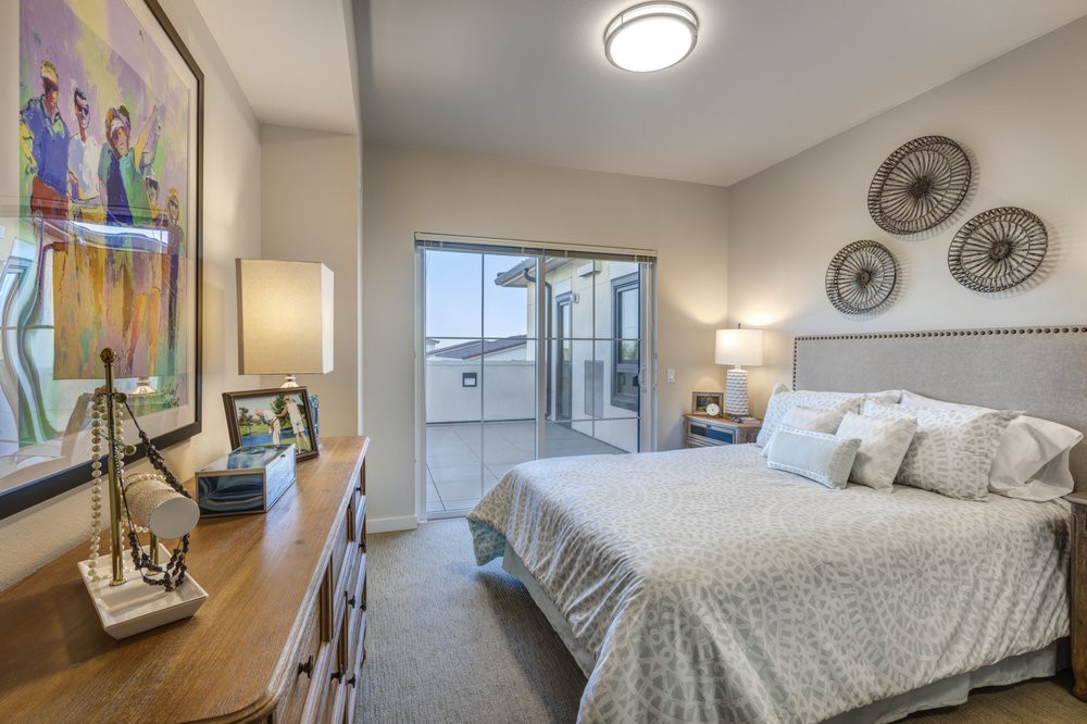 A modern bedroom with neutral decor, featuring a bed, dresser, and lamps.