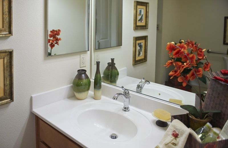 A modern bathroom with a sleek white sink, decorative vases, and vibrant orange flowers.