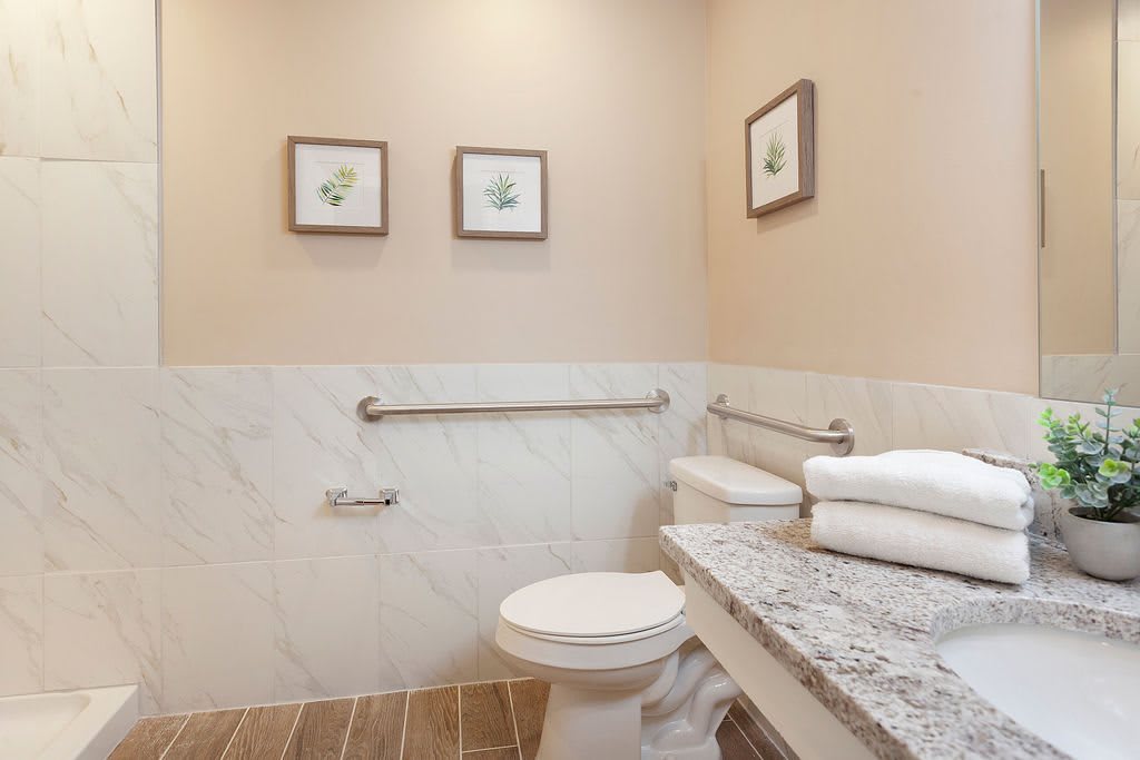 A clean bathroom with a toilet, grab bars, and neatly folded towels on a marble countertop.